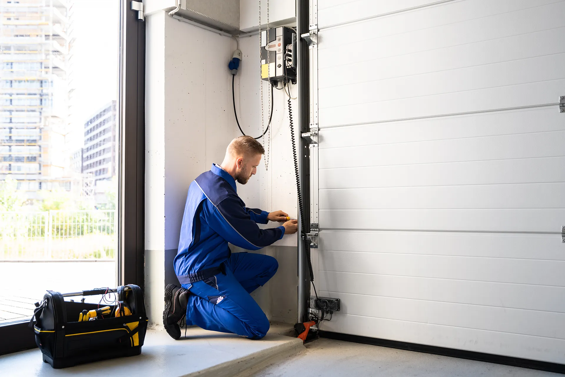 A garage door technician on his knees performing a repair on a residential garage door.