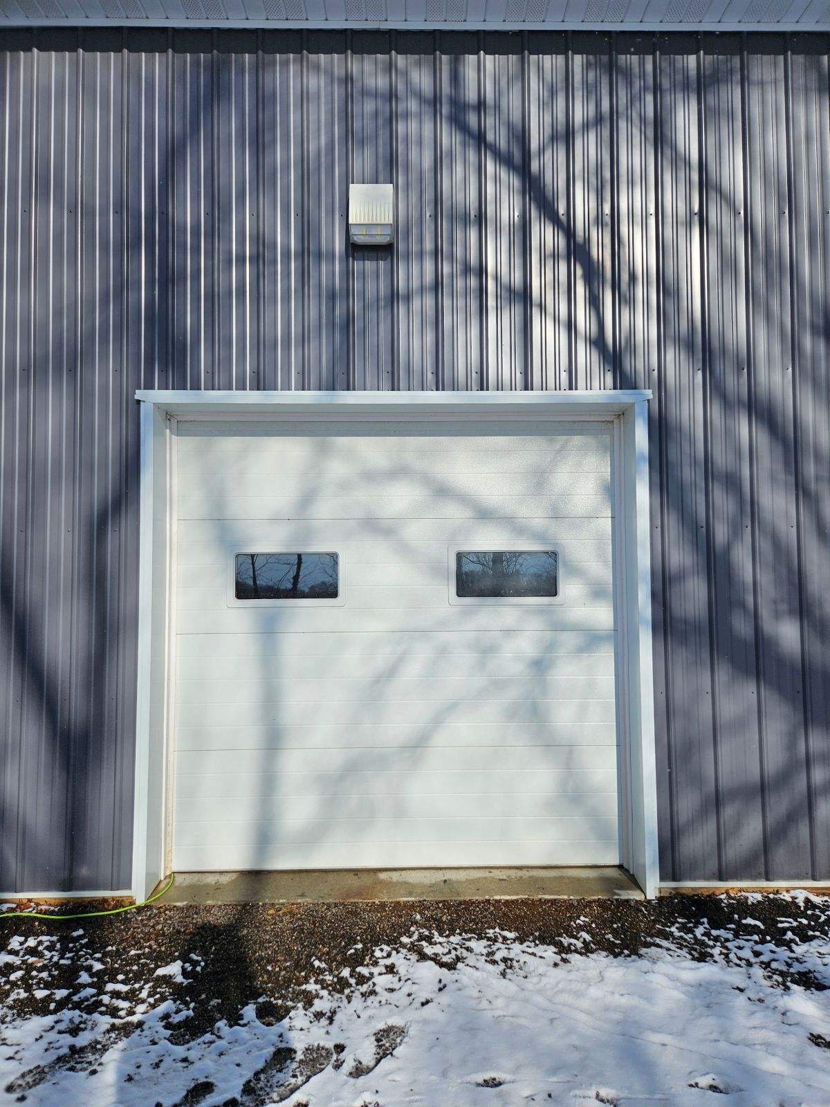 Garage door on metal building with tree shadows and snow on the ground.