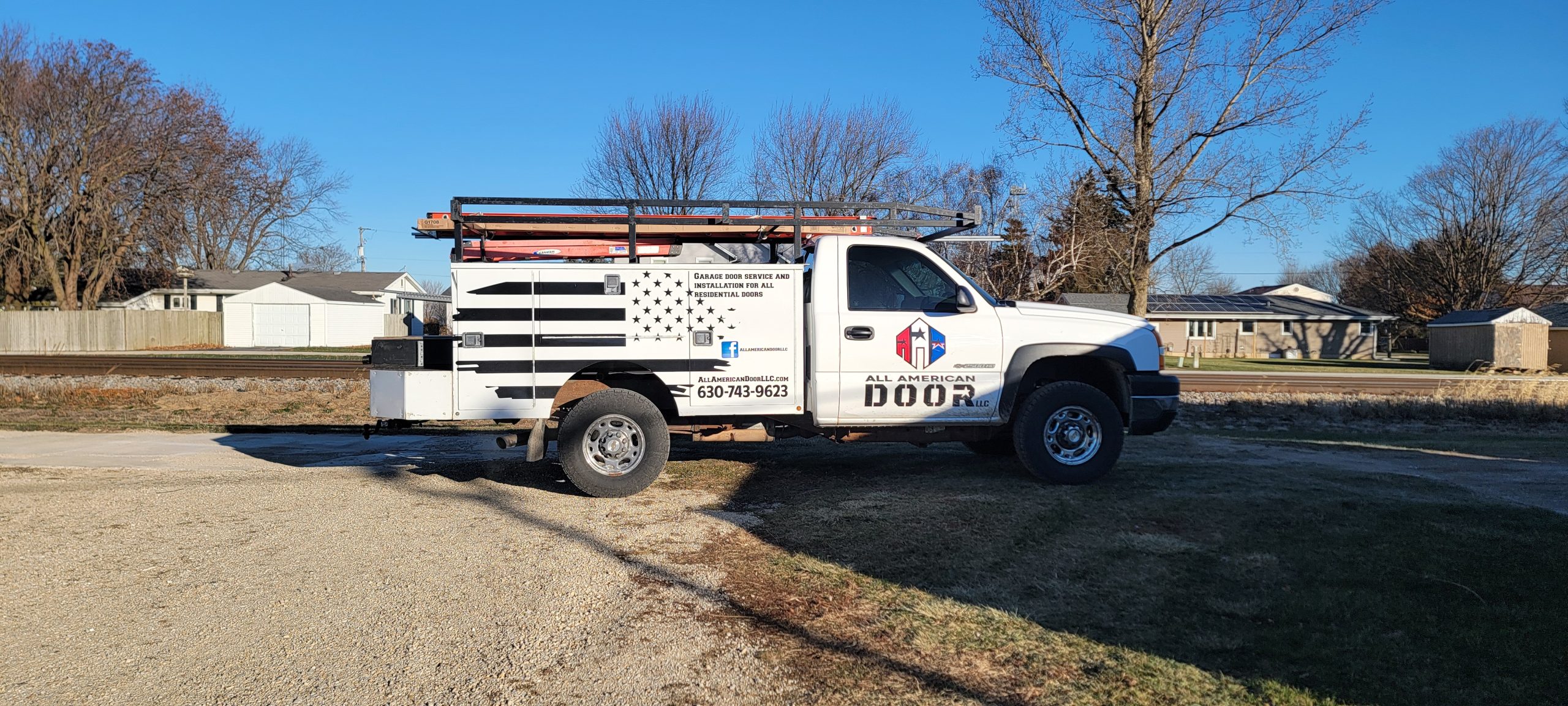 Service truck for All American Door parked on a rural road with residential background.