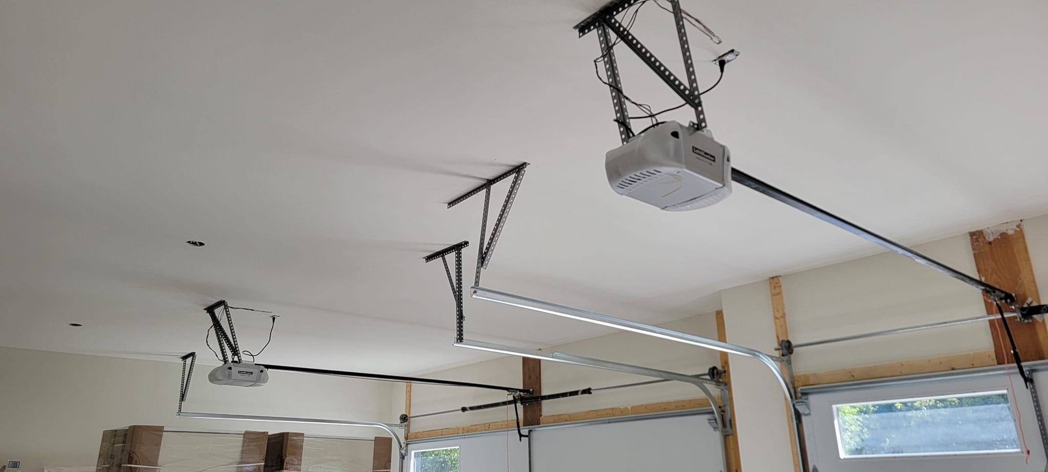 Ceiling-mounted garage door opener system with visible track and electrical wiring in a garage setting.