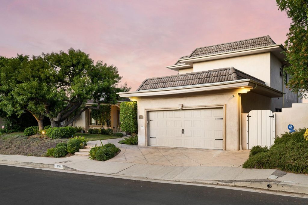 Residential garage door facing a driveway bordered with dense trees and shrubs.